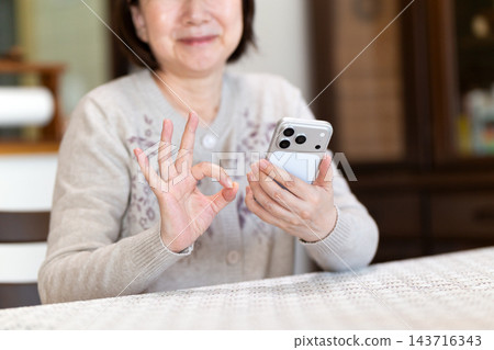 中老年女性在家裡的客廳用智慧型手機做圓週運動。 143716343