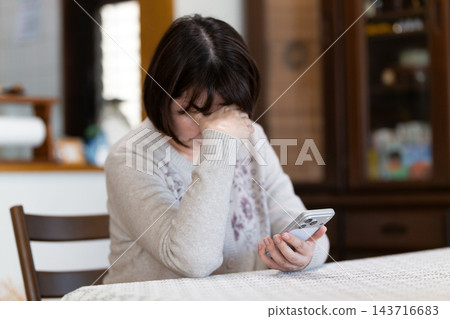 中老年女性在客廳情緒低落,手上拿著智慧型手機。 中老年女性在客廳情緒低落,手上拿著智慧型手機。 143716683