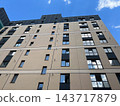 A low angle view shows a multi-story apartment building with rows of windows in a city under a blue sky during the day 143717879