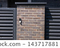 A building intercom is mounted on a brick pillar between metal gates at an entrance in daylight 143717881