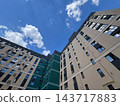New development apartment buildings rise around an inner courtyard in a city, viewed from below during the day under a blue sky 143717883