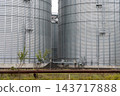 Two grain storage silos rise above tracks at an agricultural facility during the day, with no workers or rail activity visible 143717888