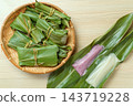 An overhead view of two-colored mochi served on a bamboo basket and long ginger lily leaves. 143719228