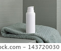White cosmetic borttle mockup on light green towel in bathroom, unbranded packaging 143720030
