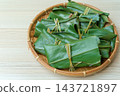 Close-up of leaf-wrapped mochi served on a bamboo basket with a wood grain pattern. 143721897
