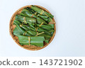 An overhead view of a bamboo basket containing mochi placed on the left side against a light-colored background. 143721902