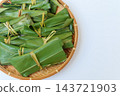 A close-up of a bamboo basket and mochi placed on the left side against a light-colored background. 143721903