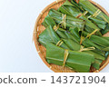 A close-up of a bamboo basket and mochi placed to the right against a light-colored background. 143721904