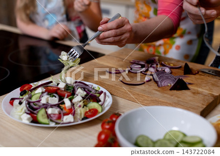 Preparing fresh Mediterranean style salad, Creating vibrant salad with vegetables and energetic atmosphere, Arranging colorful vegetables in bowl during lively kitchen moment 143722084
