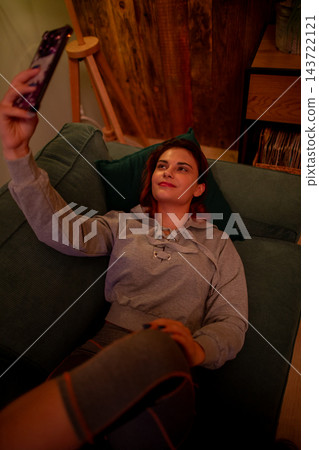 Relaxed woman captures cozy moment. Informal picture of woman relaxing at home with comfort. Casual photograph showing woman in warm environment during evening hours Relaxed woman captures cozy moment. Informal picture of woman relaxing at home with comfort. Casual photograph showing woman in warm environment during evening hours 143722121