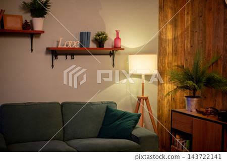 Soft green sofa beside glowing lamp curated for cozy reading, layered cushions, wall shelf dcor, potted fern, warm wooden panel backdrop, quiet evening atmosphere Soft green sofa beside glowing lamp curated for cozy reading, layered cushions, wall shelf dcor, potted fern, warm wooden panel backdrop, quiet evening atmosphere 143722141