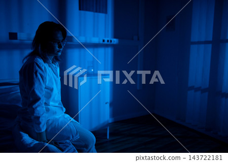 Peaceful individual by window. Relaxed person sitting calmly in bluish light environment. Serene individual positioned by window with gentle breath and composed demeanor Peaceful individual by window. Relaxed person sitting calmly in bluish light environment. Serene individual positioned by window with gentle breath and composed demeanor 143722181