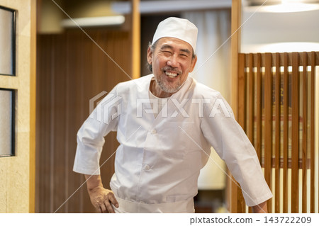 一位經驗豐富的壽司師傅面帶微笑,直視鏡頭。 一位經驗豐富的壽司師傅面帶微笑,直視鏡頭。 143722209