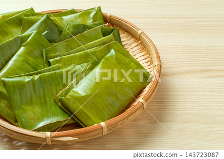 左邊是一個竹籃，裡面裝滿了用香蕉葉包裹的麻糬，周圍是空的。 143723087
