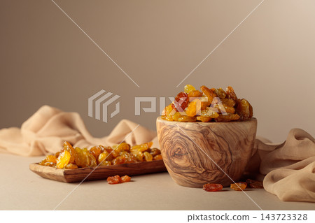 Yellow sultana raisins in a wooden bowl on a beige background. Yellow sultana raisins in a wooden bowl on a beige background. 143723328