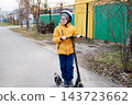 A joyful boy wearing glasses and a helmet rides a scooter along a residential street in autumn. 143723662