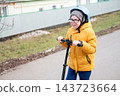 Close-up of a smiling preteen boy in helmet and glasses riding scooter outdoors in fall 143723664