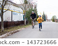 A father on a bicycle and his son on a scooter are racing along an empty paved road in a residential area in the autumn countryside. 143723666