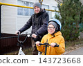 Smiling father on bicycle and son on kick scooter riding together on suburban street in autumn 143723668