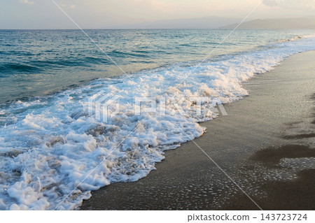 Sea wave with white foam rolling onto sandy shore Sea wave with white foam rolling onto sandy shore 143723724