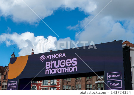 Athora Bruges Marathon finish line arch banner structure against blue sky on Grote Markt in Bruges Belgium Athora Bruges Marathon finish line arch banner structure against blue sky on Grote Markt in Bruges Belgium 143724334