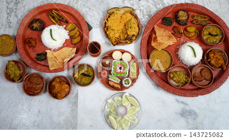Traditional Bengali thali meal spread served in terracotta clay plates and bowls featuring authentic dishes and sweets 143725082