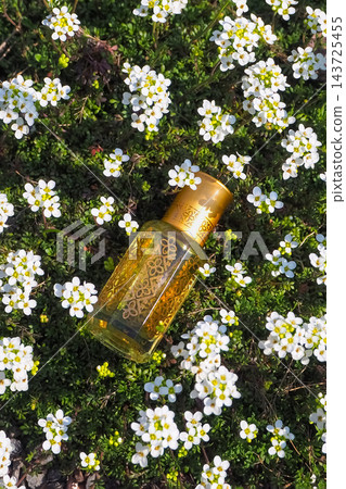 Exotic Perfume Oil Bottle Lying in a Field of Small White Flowers 143725455