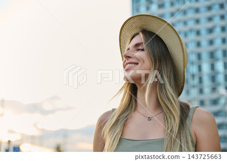 Happy young woman in straw hat eyes closed smiling outdoors city portrait Happy young woman in straw hat eyes closed smiling outdoors city portrait 143725663