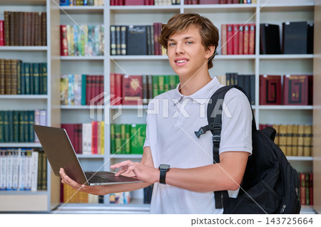 Teenage boy student using laptop with backpack in library portrait Teenage boy student using laptop with backpack in library portrait 143725664