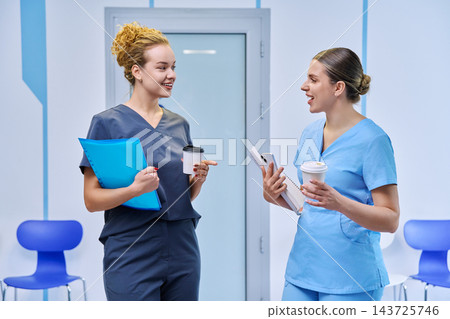 Two young medical interns talking with coffee in hospital corridor shot Two young medical interns talking with coffee in hospital corridor shot 143725746