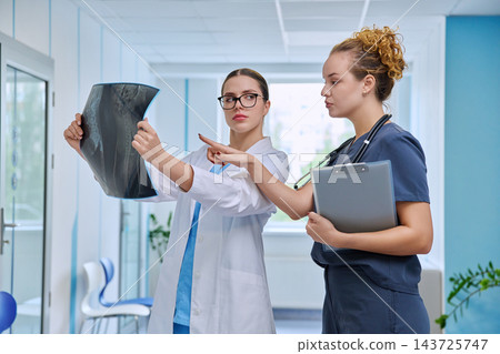 Two female doctors examining x-ray image standing in modern clinic corridor Two female doctors examining x-ray image standing in modern clinic corridor 143725747