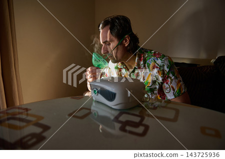 Man using nebulizer mask at home for breathing treatment and respiratory therapy Man using nebulizer mask at home for breathing treatment and respiratory therapy 143725936
