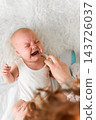Baby 5-6 months old cries while mother puts on a white bodysuit at home, authentic everyday baby care 143726037