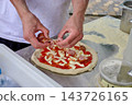 A cook adds cheese and toppings to a pizza at a work table in a kitchen during food preparation 143726165