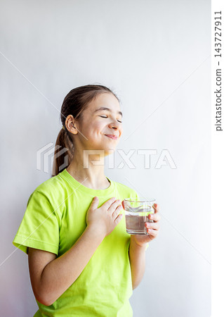 Young girl in green shirt holding a glass of water with a grateful smile and hand on chest Young girl in green shirt holding a glass of water with a grateful smile and hand on chest 143727911
