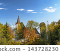 Historic Church Tower Peeking Through Autumn Trees Under A Bright Blue Sky In Rural Landscape 143728230