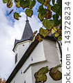 Autumn Church Steeple Framed by Golden Leaves Against a Cloudy Blue Sky 143728234
