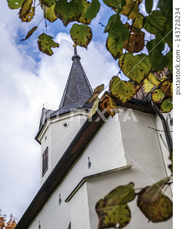 Autumn Church Steeple Framed by Golden Leaves Against a Cloudy Blue Sky Autumn Church Steeple Framed by Golden Leaves Against a Cloudy Blue Sky 143728234