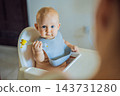 Infant learning to use a feeding fork with mother beside the table with pineapple. 143731280