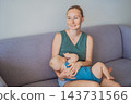 Mother feeding her infant at the breast on a living room sofa. 143731566