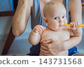Infant exploring a toothbrush while mother demonstrates toothbrushing. 143731568