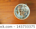 Grilled meat and rice topped with sesame seeds in a round takeout container on a wooden table. High angle view of a convenient packaged meal. 143733375