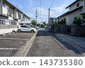 一輛白色汽車停在公寓大樓的停車場，陽台上晾曬著衣物，日本住宅區的一條狹窄街道兩旁豎立著電線桿和電線。 143735380