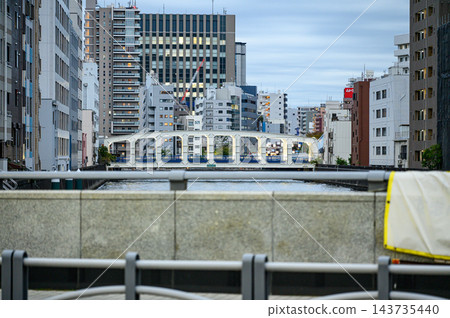 一座白色橋樑橫跨摩天大樓林立的城市中的一條水道,橋樑上有一系列拱形開口,透過欄桿可以看到陰雲密佈的城市景觀。 一座白色橋樑橫跨摩天大樓林立的城市中的一條水道,橋樑上有一系列拱形開口,透過欄桿可以看到陰雲密佈的城市景觀。 143735440