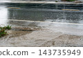 Close up view of a wet asphalt road surface. During heavy rain with puddles water splashes and driving reflections. Water flowing from higher ground onto the road. 143735949