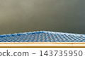Blue tiled roof edge viewed against an overcast gray rainy sky. With a soft atmospheric mood during a wet weather day. Suitable for illustrating protection against rainfall. 143735950