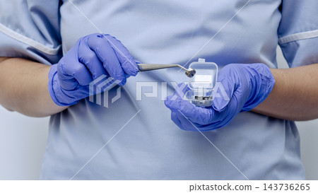 Dentist presenting metal tooth crowns in a small container as part of dental restoration preparation 143736265