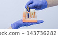 Dental implant model with removable abutment held in blue gloved hands against a light background 143736282