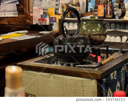 A cast iron kettle sits over charcoal in a long brazier, and the interior of a charming Japanese-style izakaya (pub). A cast iron kettle sits over charcoal in a long brazier, and the interior of a charming Japanese-style izakaya (pub). 143736723