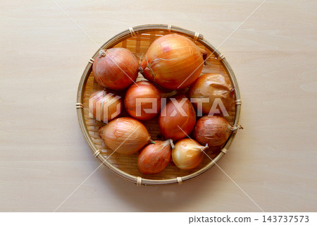 A table background viewed from directly above: imperfect, irregularly shaped onions served in a colander. A table background viewed from directly above: imperfect, irregularly shaped onions served in a colander. 143737573